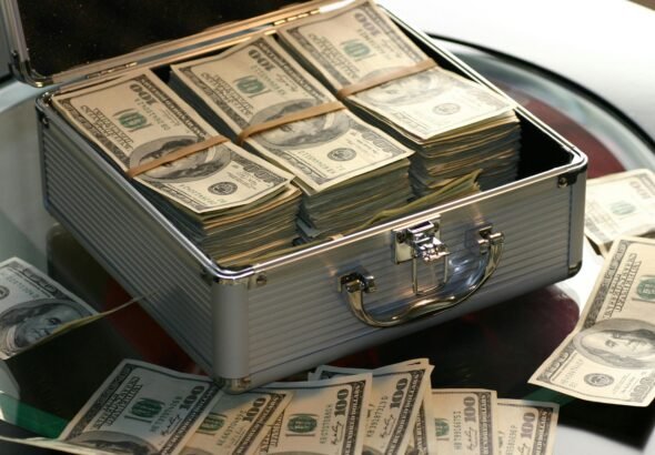 Open briefcase filled with stacks of hundred dollar bills on a glass table, representing wealth.