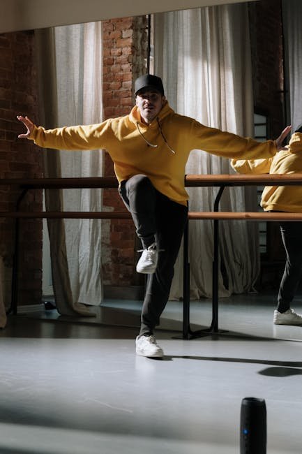 Energetic hip hop dancer in a yellow sweater striking a pose indoors with brick wall backdrop.