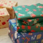 Stack of colorful Christmas gift boxes with festive wrapping paper featuring snowflakes, Santa, and stockings.