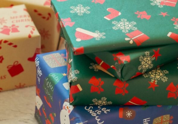 Stack of colorful Christmas gift boxes with festive wrapping paper featuring snowflakes, Santa, and stockings.